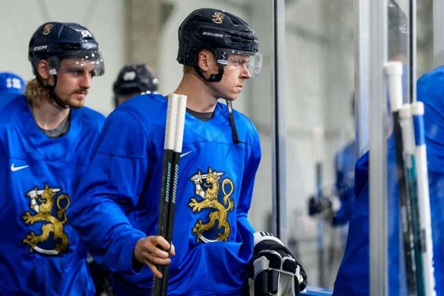 Leijonien pelaajat sinisissä harjoituspaidoissa jääkaukalon laidalla Milano-Cortinan 2026 olympialaisiin valmistautumassa. Kaksi pelaajaa katselee eteenpäin, taustalla joukkuekavereita.