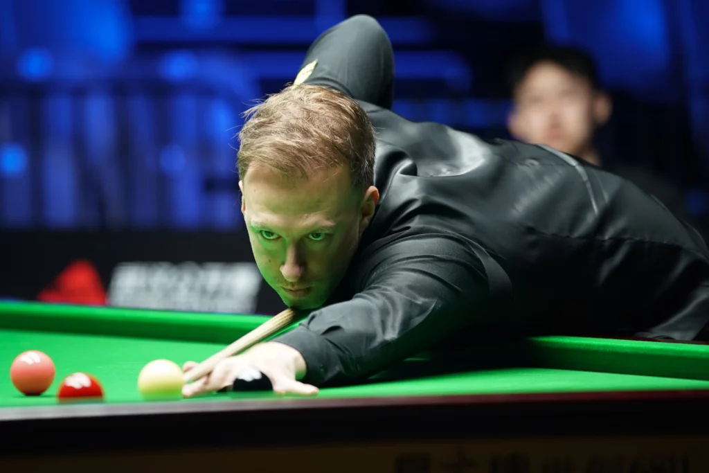 Snooker-pelaaja Judd Trump tähtää lyöntiään vihreän veran yllä musta paita päällään.