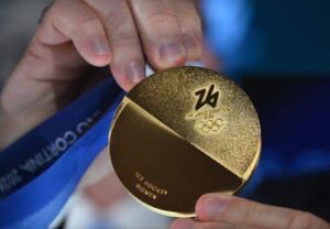 Henkilö pitelee kädessään Milano Cortina 2026 -talviolympialaisten kultamitalia, jossa lukee "Ice Hockey Women"