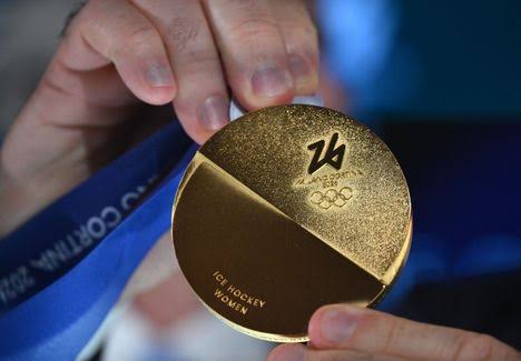 Henkilö pitelee kädessään Milano Cortina 2026 -talviolympialaisten kultamitalia, jossa lukee "Ice Hockey Women"