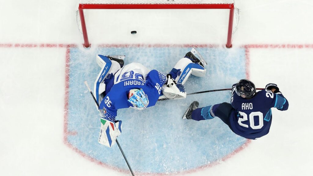 Top-down view of Finland vs Italy Olympic ice hockey game, Sebastian Aho shooting against Italian goalie in blue crease