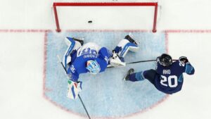 Top-down view of Finland vs Italy Olympic ice hockey game, Sebastian Aho shooting against Italian goalie in blue crease